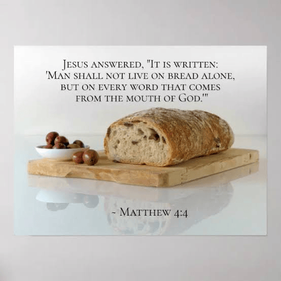 A loaf of bread on a wooden cutting board with a small dish of olives beside it. The background features a quote from Matthew 4:4 about sustenance and faith.