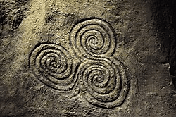 Ancient spiral petroglyph depicting three spirals interconnected on a stone surface.