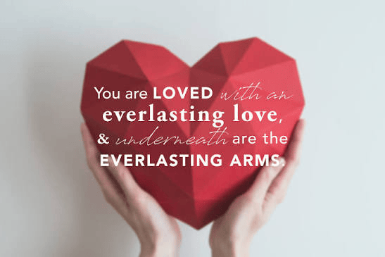A person holding a large, geometric red heart with text that reads, 'You are LOVED with an everlasting love, & underneath are the EVERLASTING ARMS.'